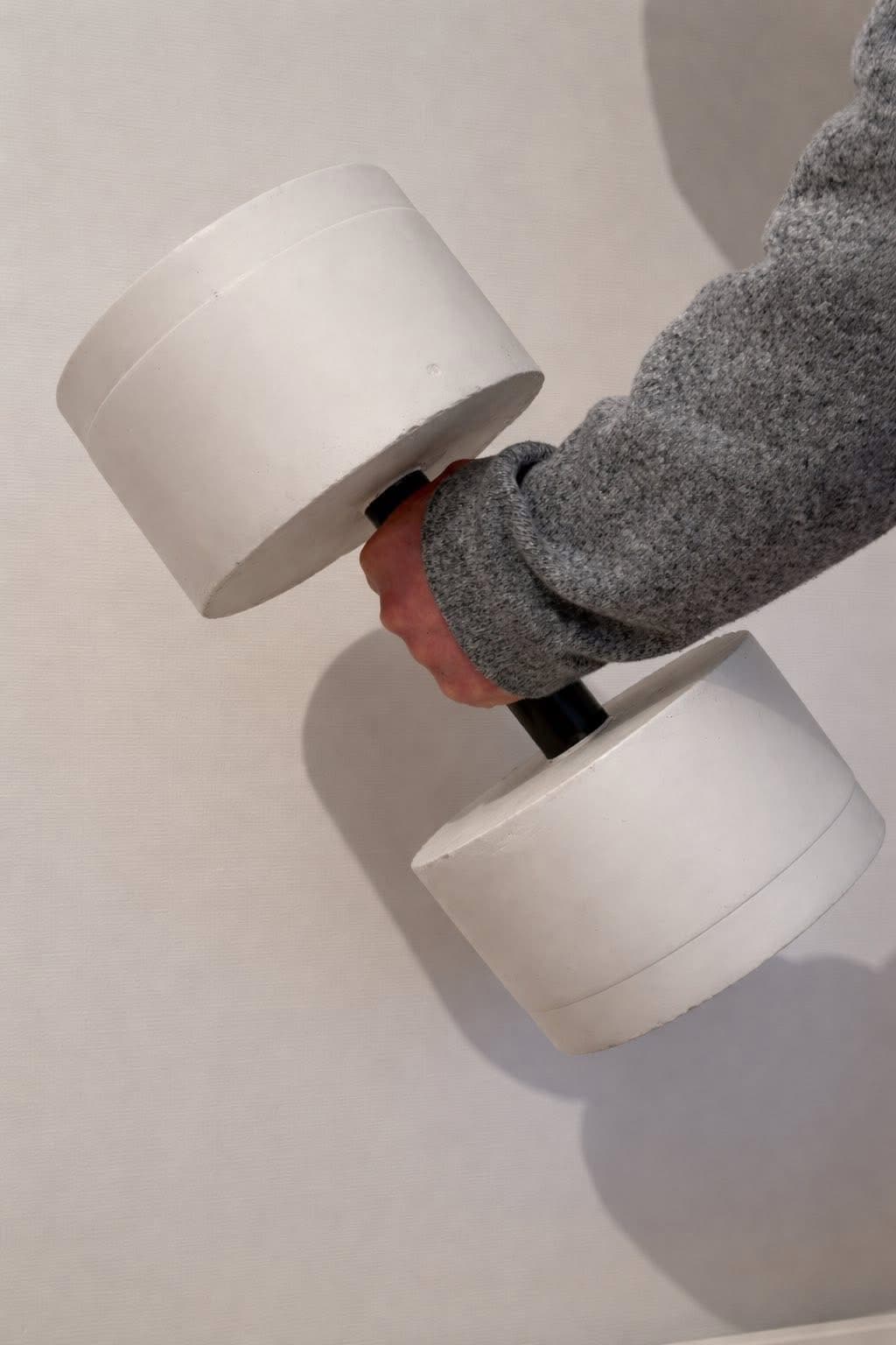 Hand holding a cast concrete dumbbell against a light wall