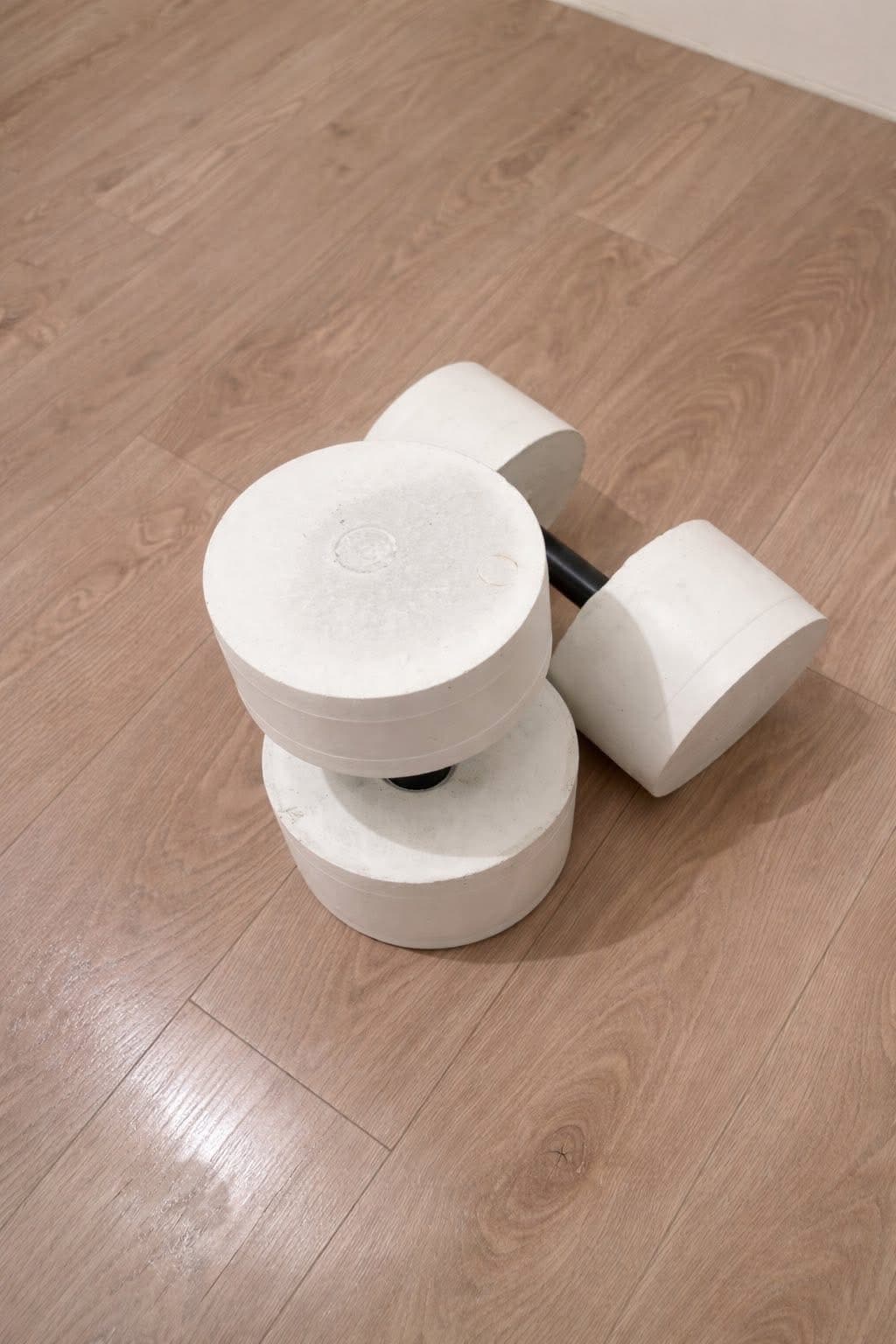 Pair of white concrete dumbbells with black handles on wood